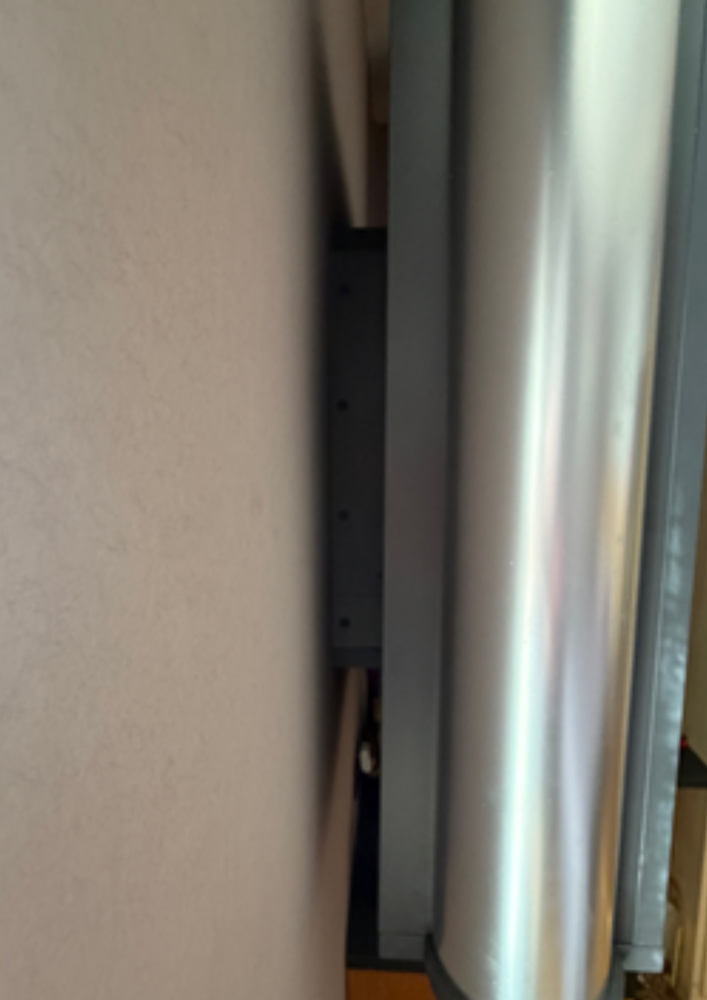 media wall pillars side view. Narrow view between a beige wall and a vertical metal surface, with a dark interior gap visible between them.